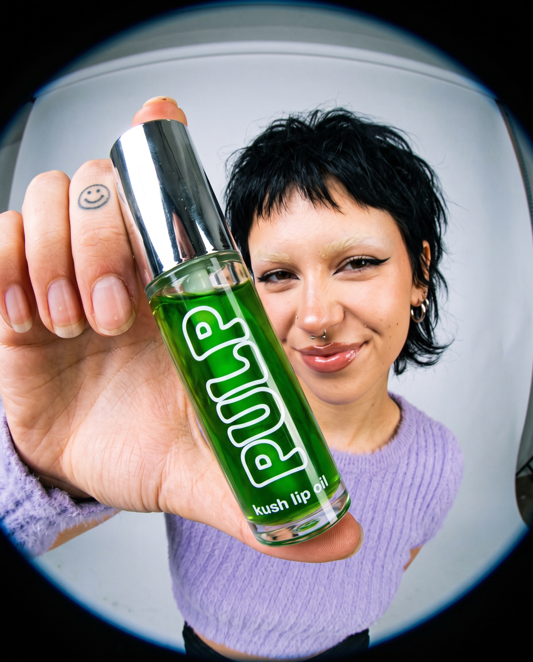 Model holding a green PULP kush lip oil toward a fisheye lens
