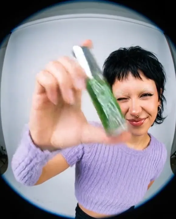 Model holding a green PULP kush lip oil toward a fisheye lens