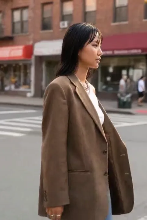 Woman in a brown blazer walking through a city intersection in daylight