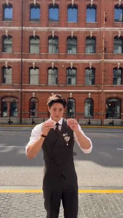 Man in a black waistcoat dancing on a cobblestone street in front of a red-brick building