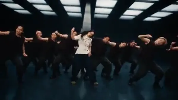 Dance crew performing in a dark studio with a grid of ceiling lights