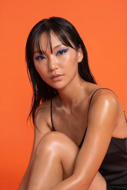 Beauty portrait with blue graphic eyeliner against an orange backdrop