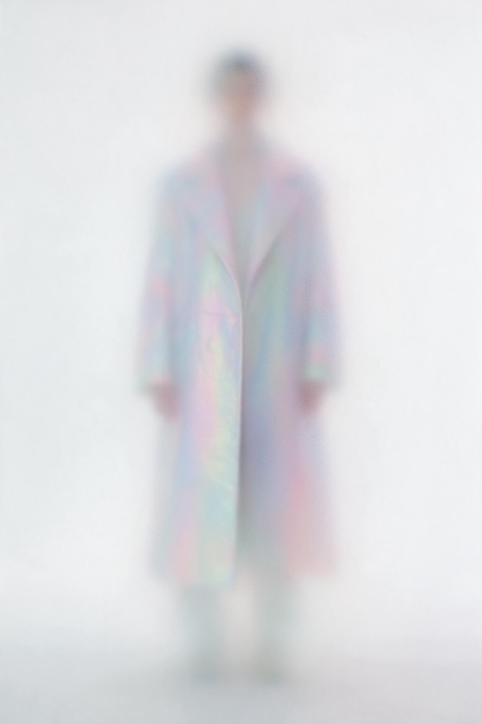 Ghostly blurred figure in an iridescent pastel coat in a white void