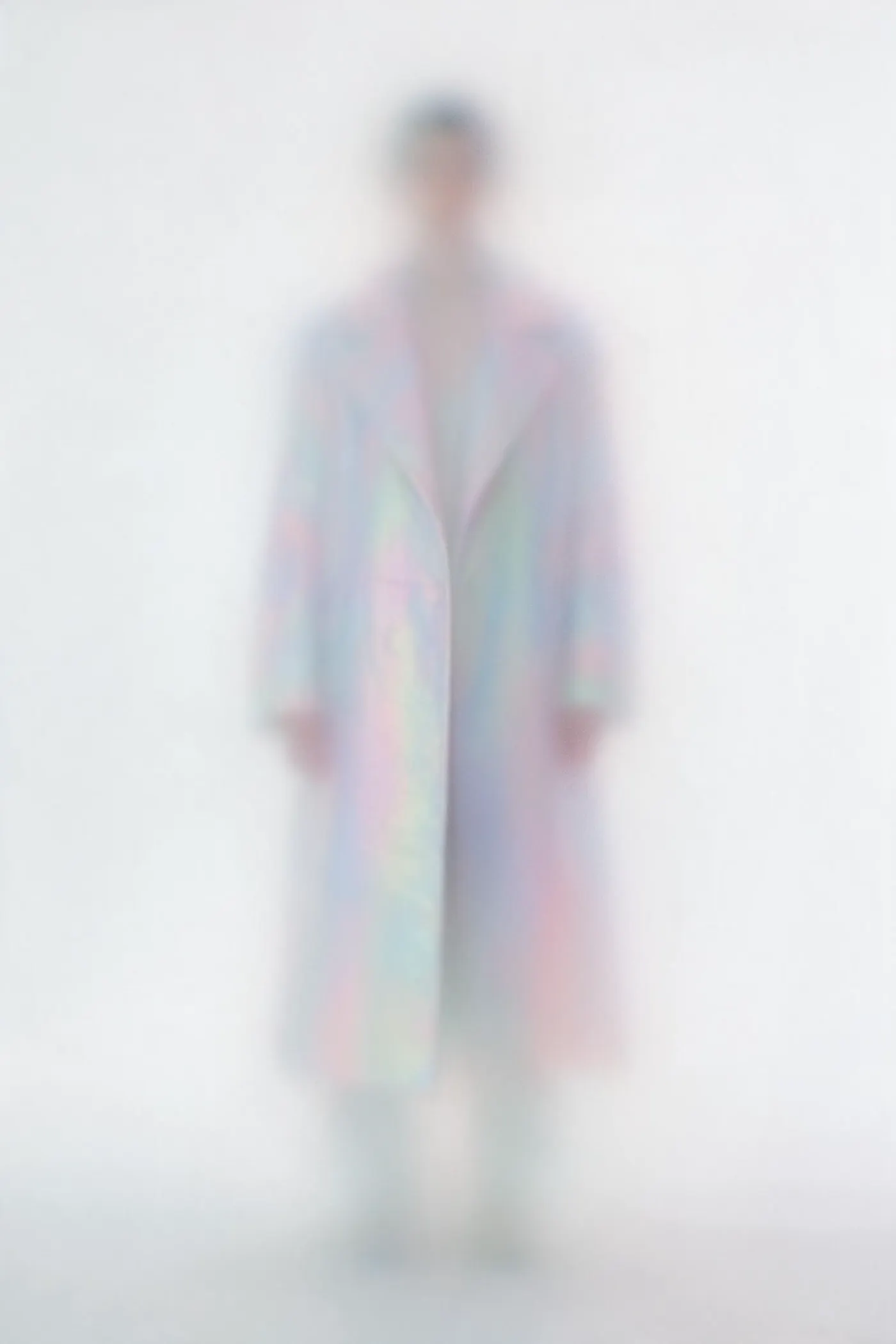 Ghostly blurred figure in an iridescent pastel coat in a white void