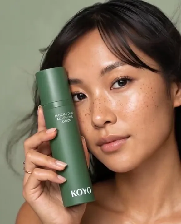 Freckled model holding a green KOYO matcha lotion bottle beside her face