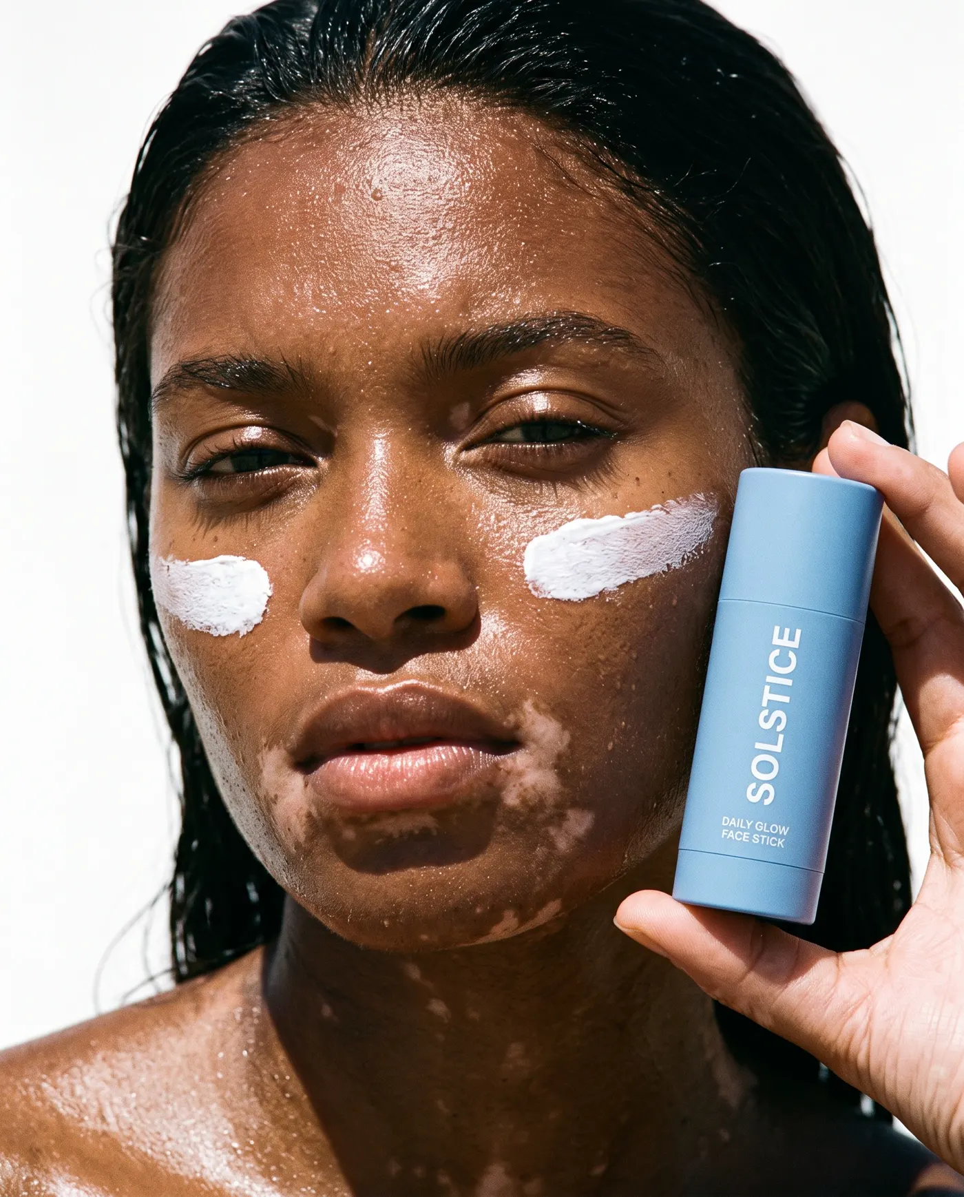Model with vitiligo and sunscreen streaks holding a blue SOLSTICE face stick